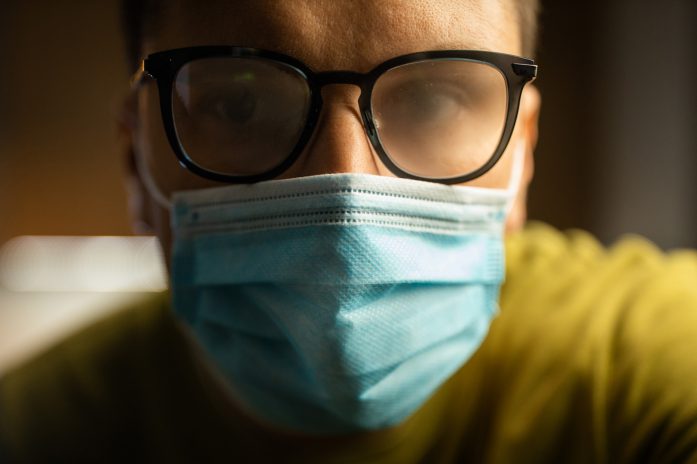 Person wearing protective mask and glasses with foggy lenses.