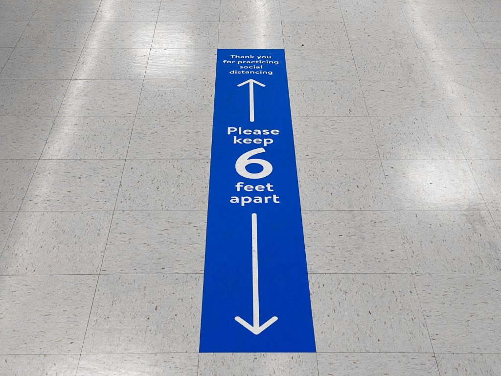 Decal stating social-distancing guidelines on aisle floor.