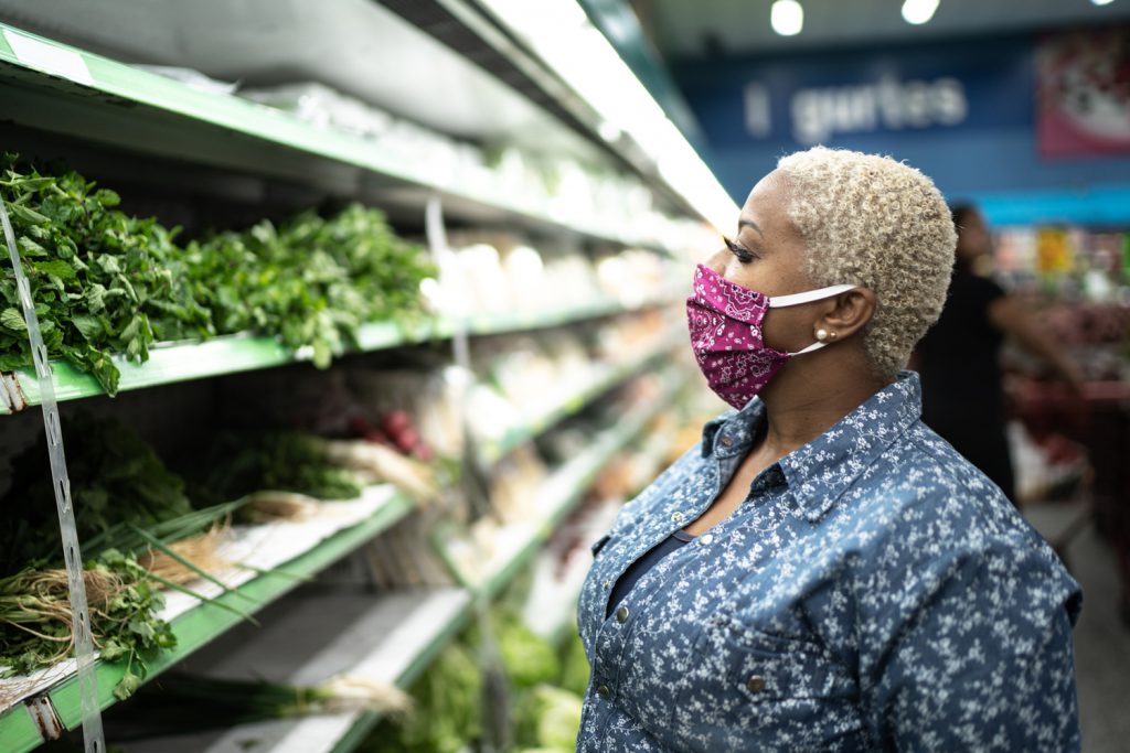 Woman looks at produce while wearing protective mask in grocery store.