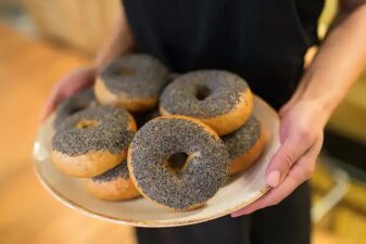 A person holding a plate of everything bagels with poppy seeds on them