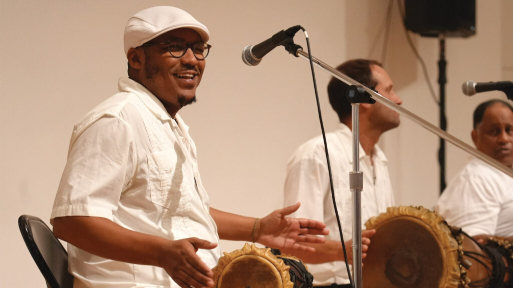 Oşubi Craig playes drums on stage at a performance with fellow drummers.
