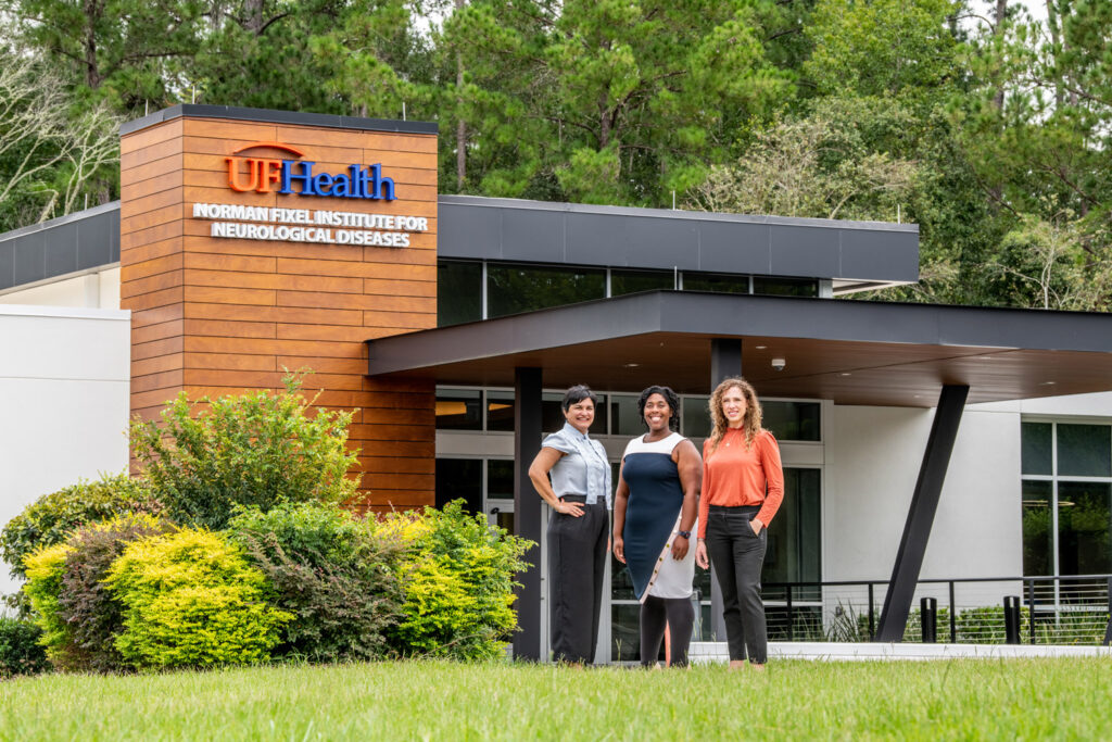 Aysegul Gunduz, Ashley Rawls and Aliyah Snyder stand outside the entrance of the UF Health Norman Fixel Institute for Neurological Diseases.
