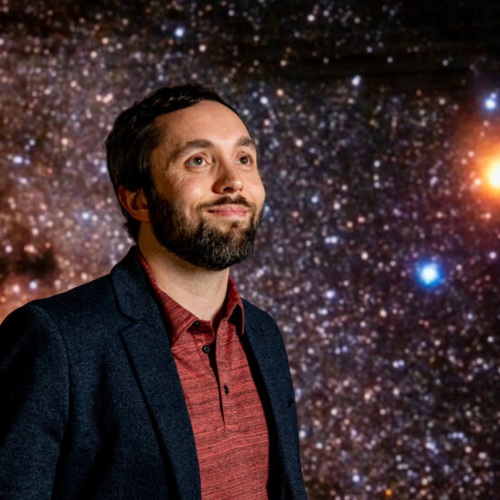 Portrait of Jason Dittmann standing in front of a screen showing a starry backdround.