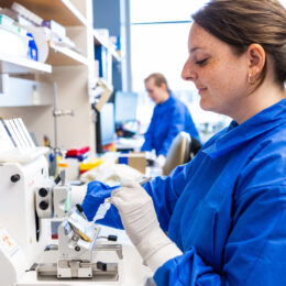 A photo of a woman in a blue lab jacket doing work in the lab.