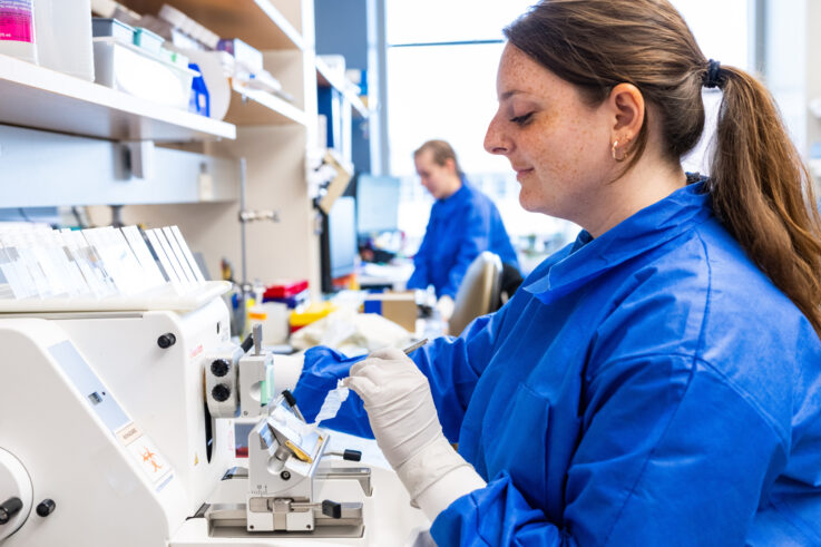 A photo of a woman in a blue lab jacket doing work in the lab.