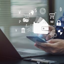 An image of human hands holding a phone with cash app logos above it and a laptop sitting open on a desk.